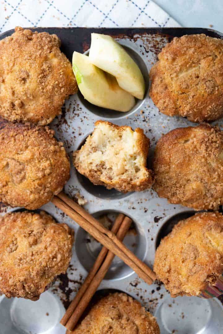Muffins in the tray with cinnamon sticks and apple slices.