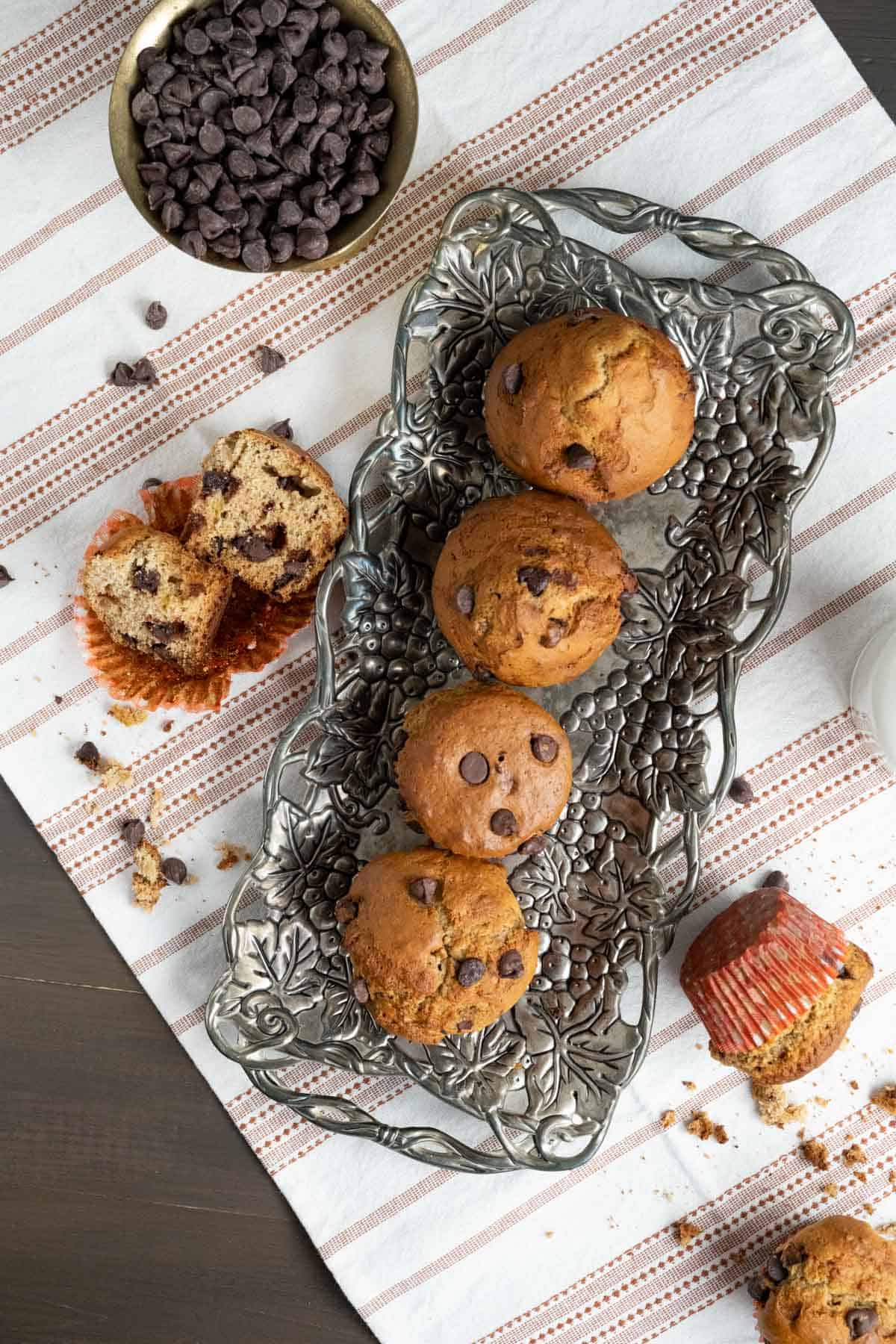 four chocolate chip banana muffins placed on a carved silver tray.