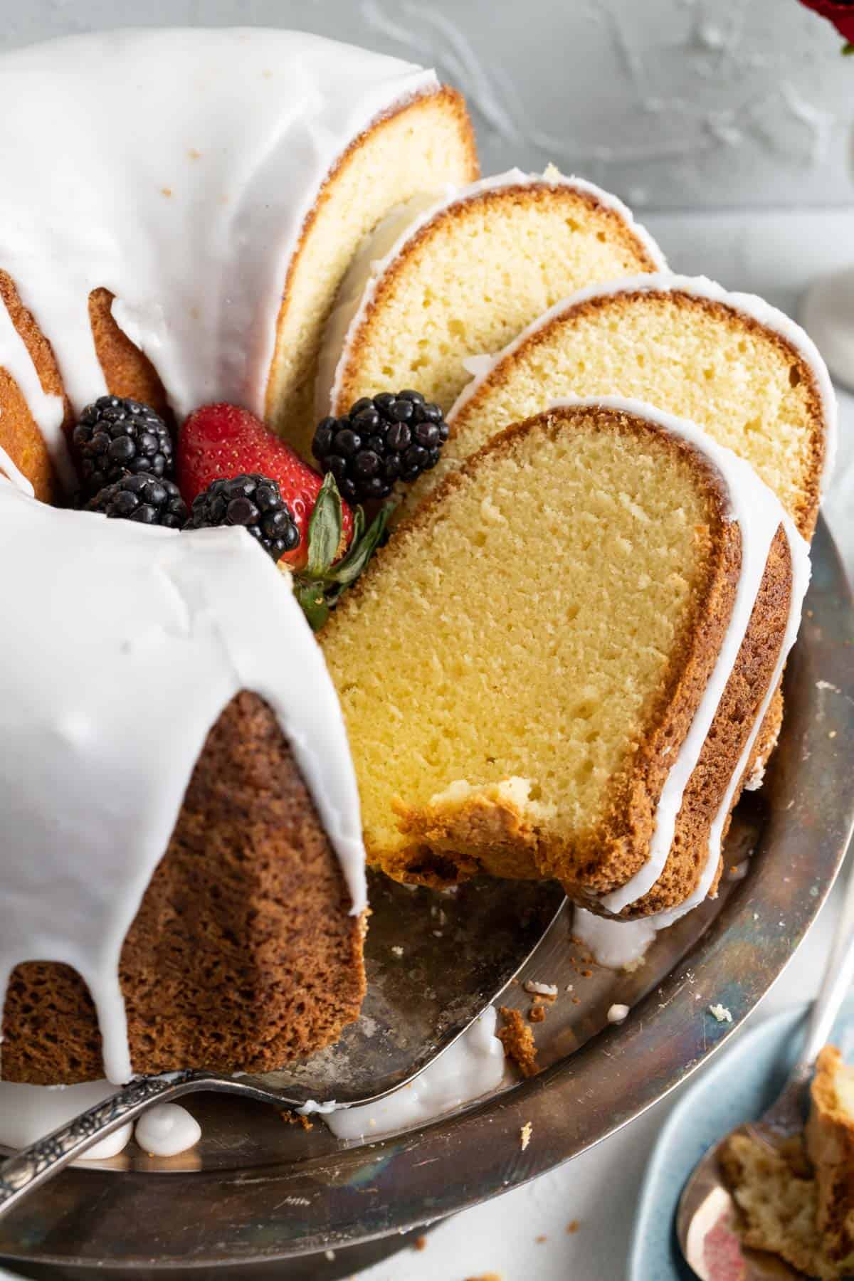old fashioned sour cream pound cake  with icing slices in a cake plate with golden spoon.