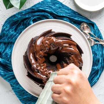 overhead shot of dark chocolate bundt cake with a pitcher pouring ganache over it.