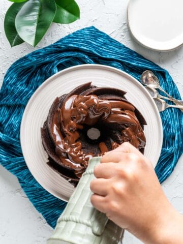 overhead shot of dark chocolate bundt cake with a pitcher pouring ganache over it.