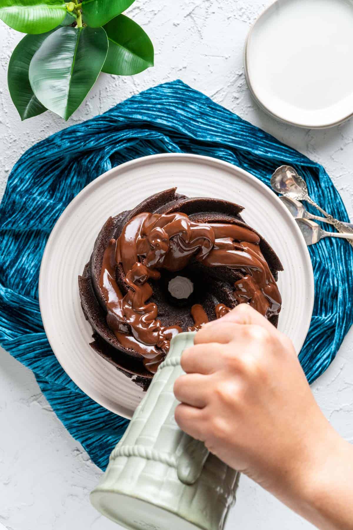 overhead shot of dark chocolate bundt cake with a pitcher pouring ganache over it. 