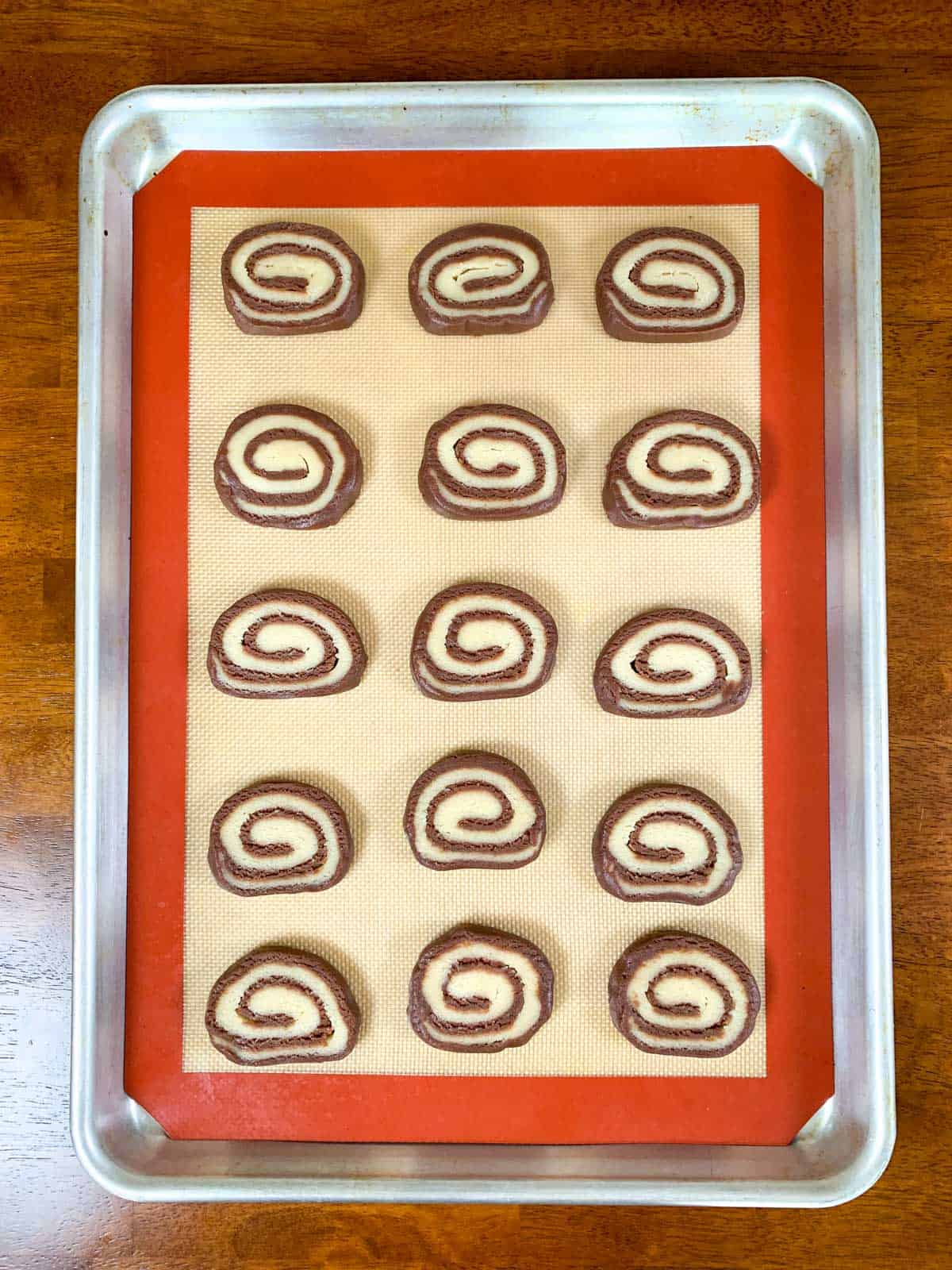 12 cut pinwheel cookies placed on a silicone mat in a baking tray.