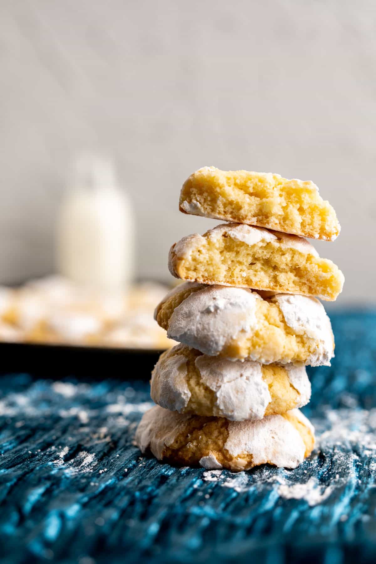 stacked lemon crinkle cookies on blue crinkled table cloth and a milk bottle in the backdrop.