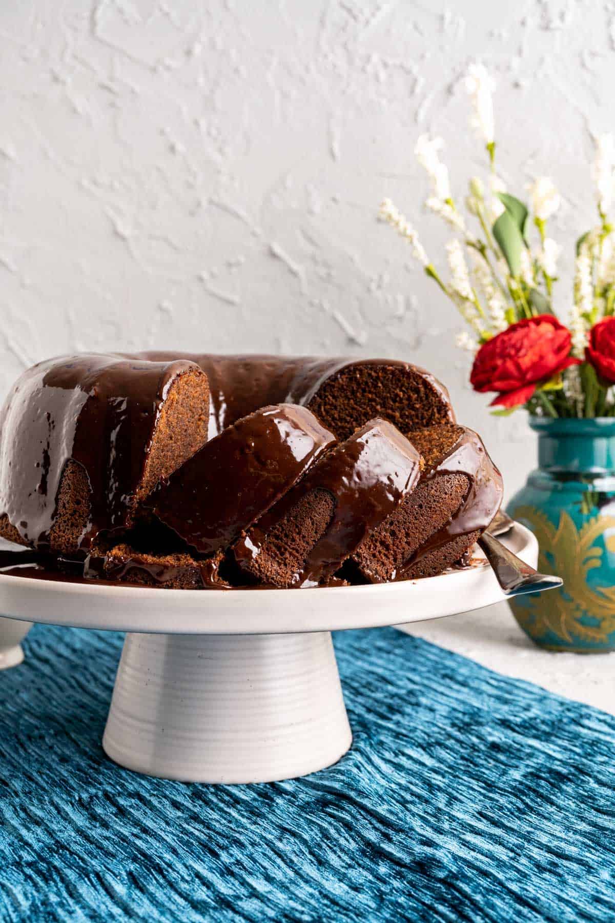chocolate sour cream pound cake on a white cake plate with flowers in the backdrop.