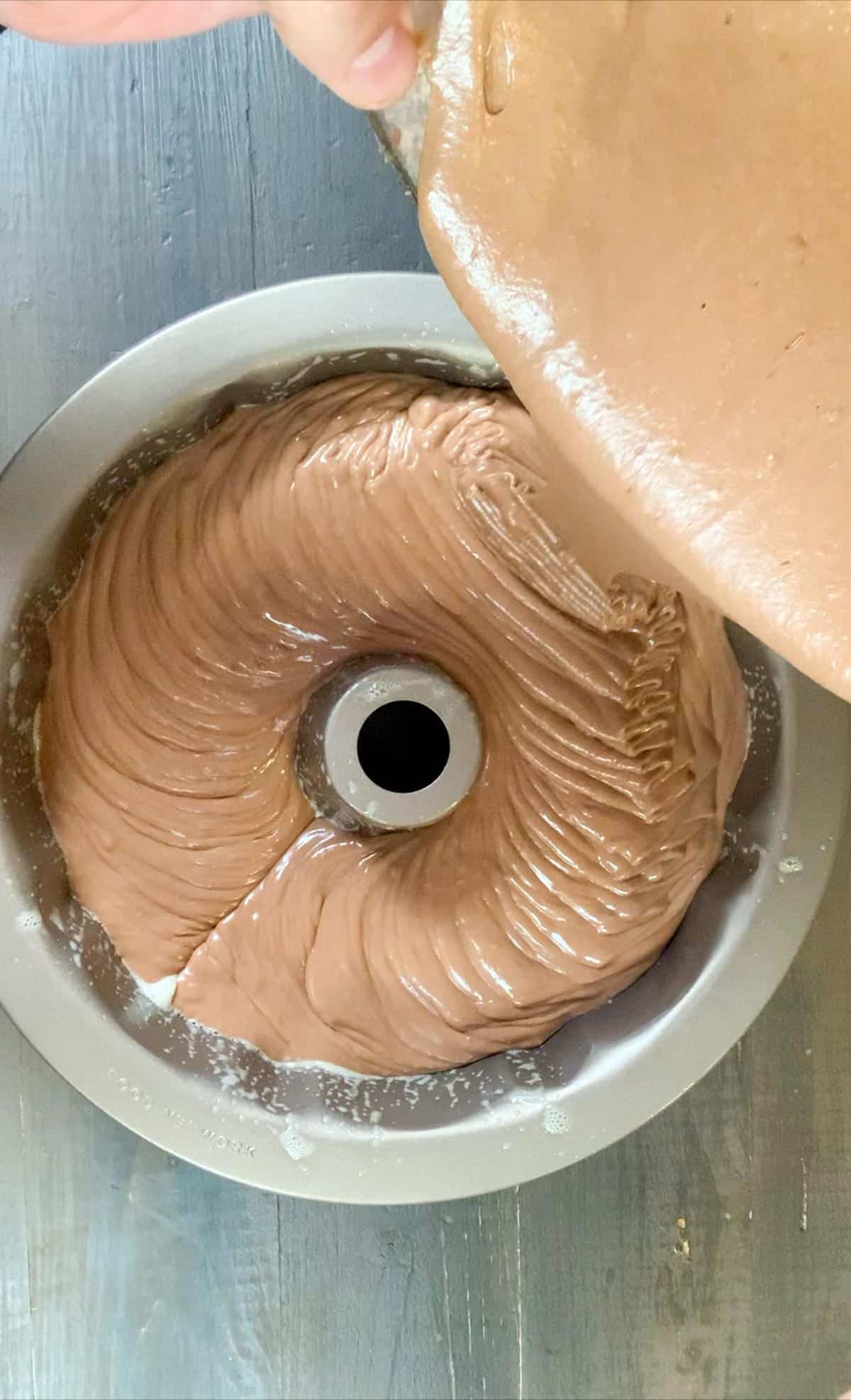 pouring the chocolate sour cream pound cake batter into the bundt pan.