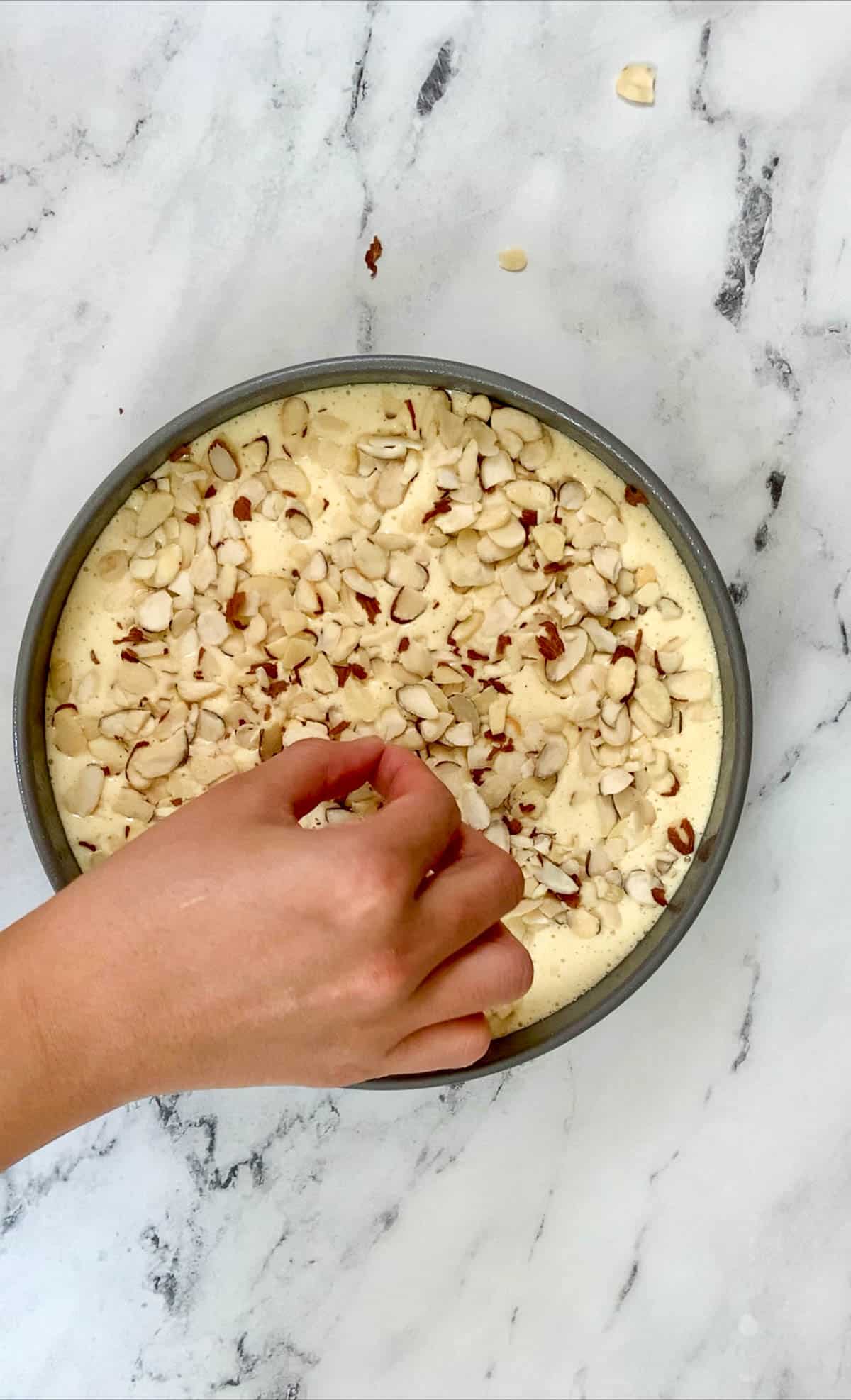 decorating the italian almond cake with slivered almonds before placing the cake in the oven.