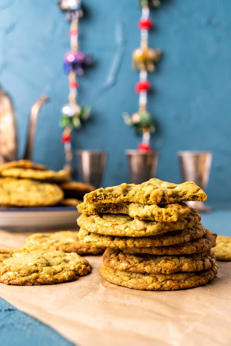 seven matcha cookies stacked over each another on a brown paper with three tea cups in the backdrop.