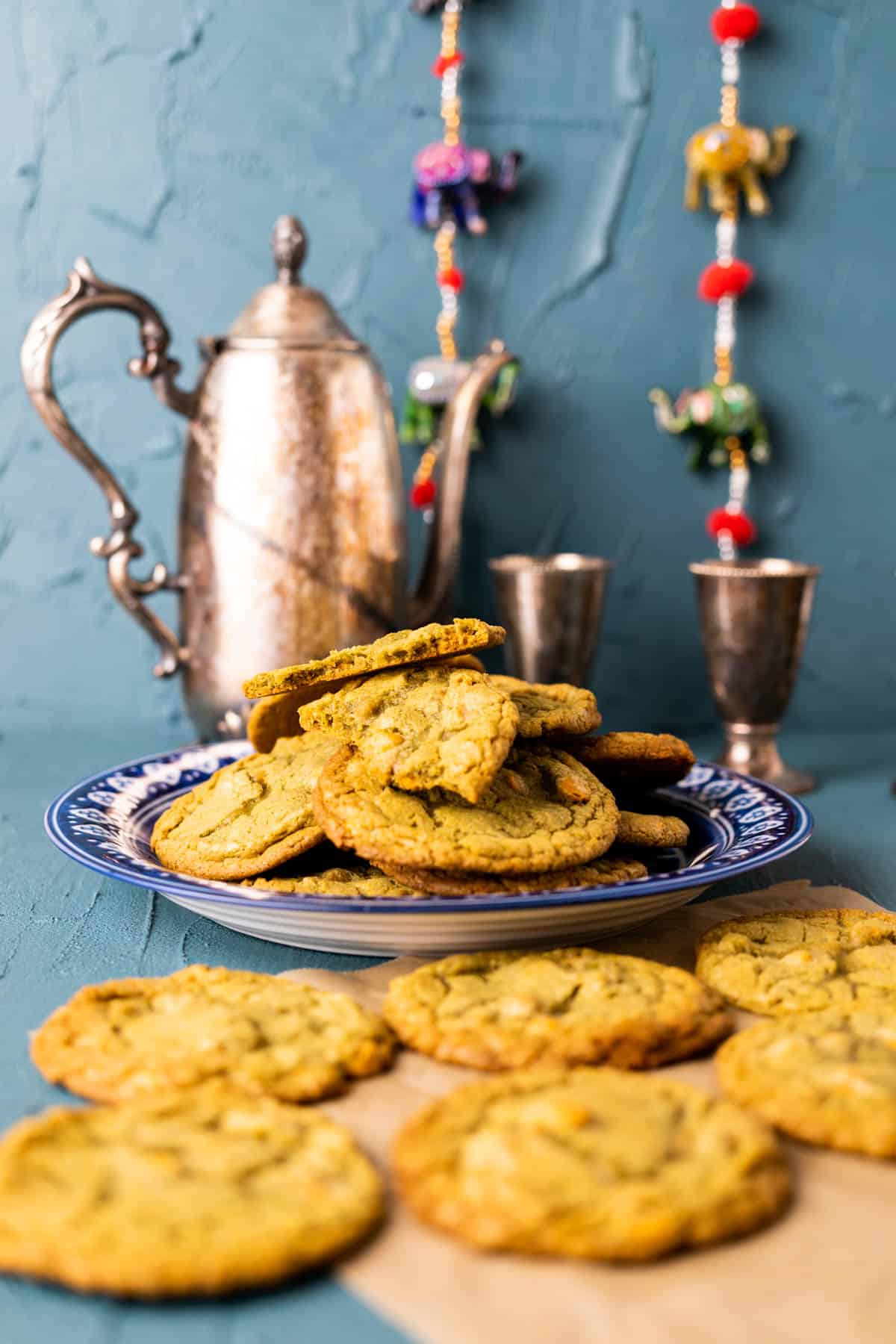 close shot of the matcha cookies in blue plate with silver tea pot in the backdrop.