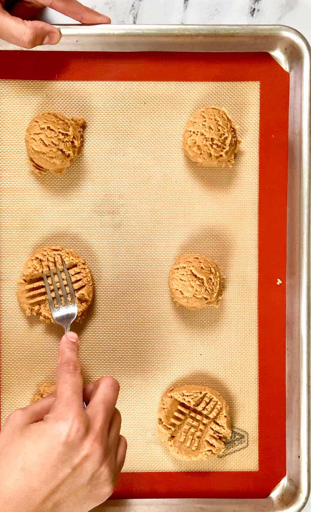 Pressing and shapring the criss cross design on the almond flour cookies dough balls.