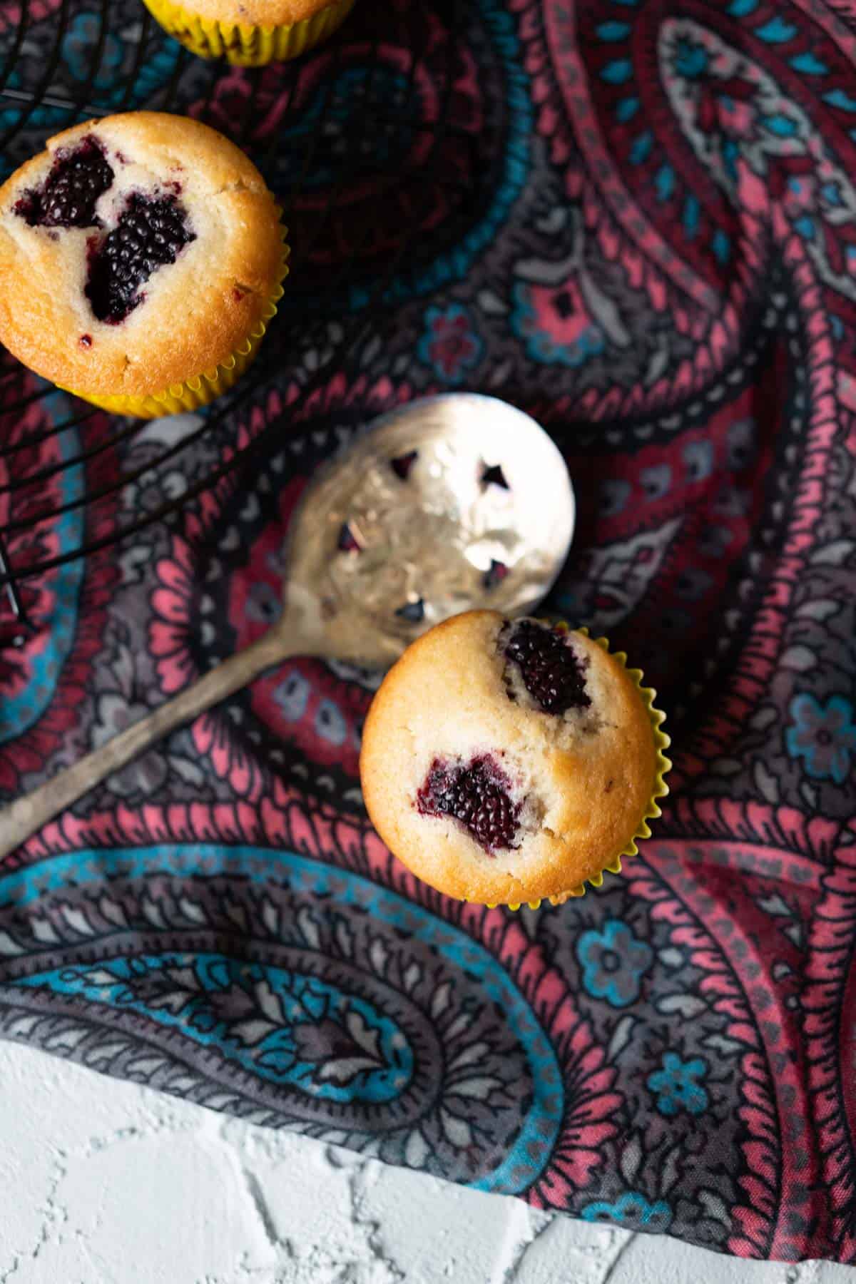 Vegan blackberry muffin sitting on a gray table cloth with golden spoon on the side.