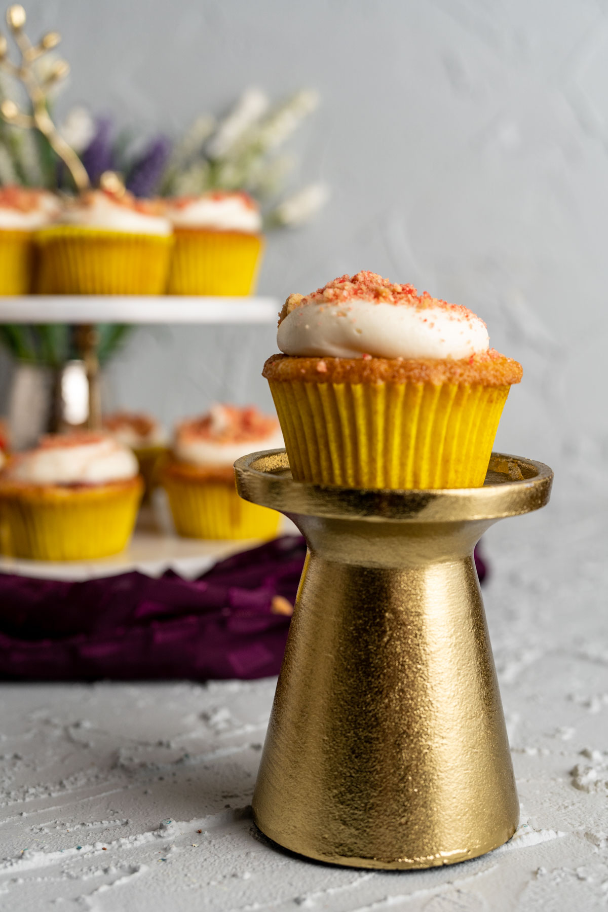 cupcake sitting on a golden stand with other cupcakes in the backdrop.