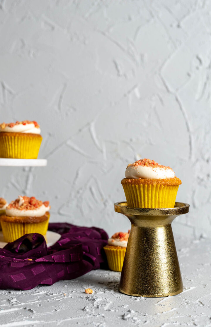 strawberry crunch cupcake sitting on a golden stand with other cupcakes in the backdrop.