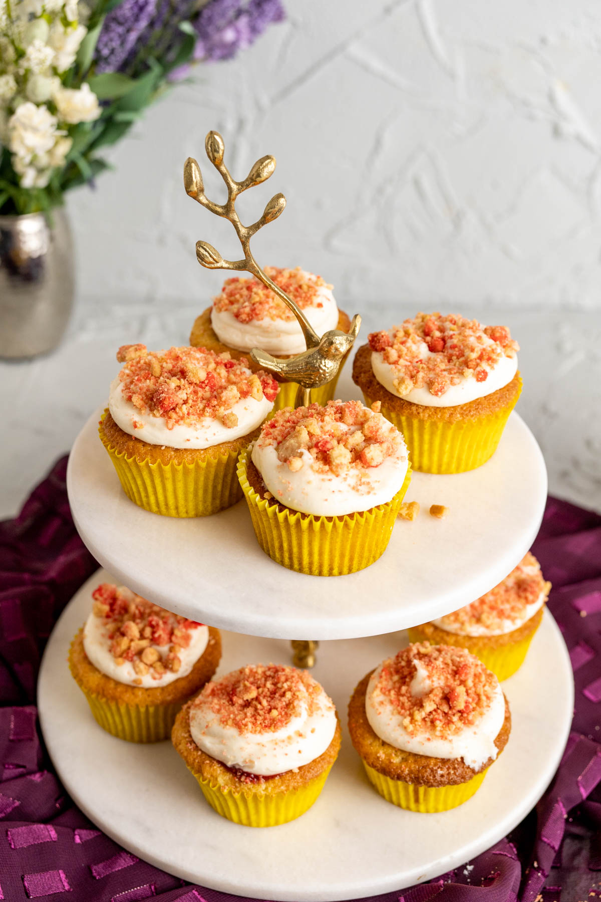 strawberry crunch cupcakes on a white cupcake stand with flowers in the backdrop.