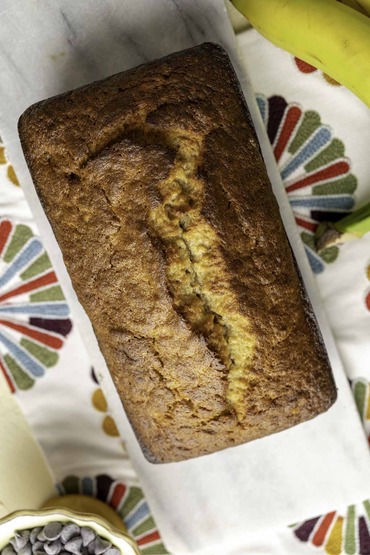 the whole loaf of a baked banana bread without baking soda placed on a decorative marble slab.