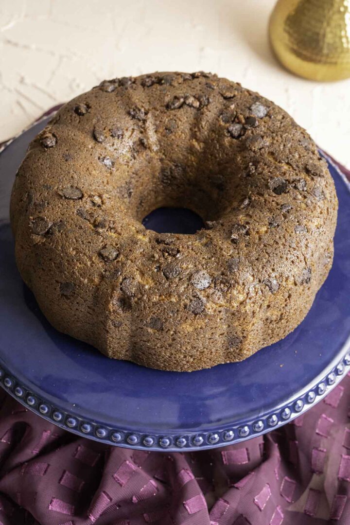 whole banana chocolate chip bundt cake sitting on the navy blue cake stand with a golden flower vase in the background.