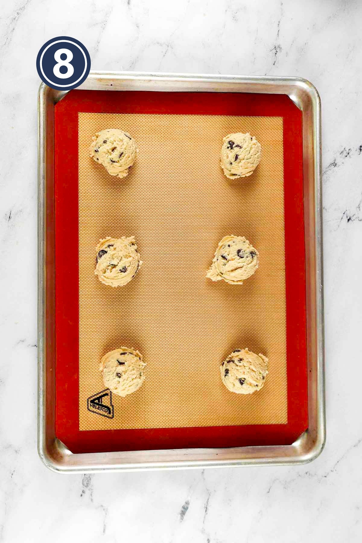 six scooped out chocolate chip cookies placed over silicone mat in a baking tray.