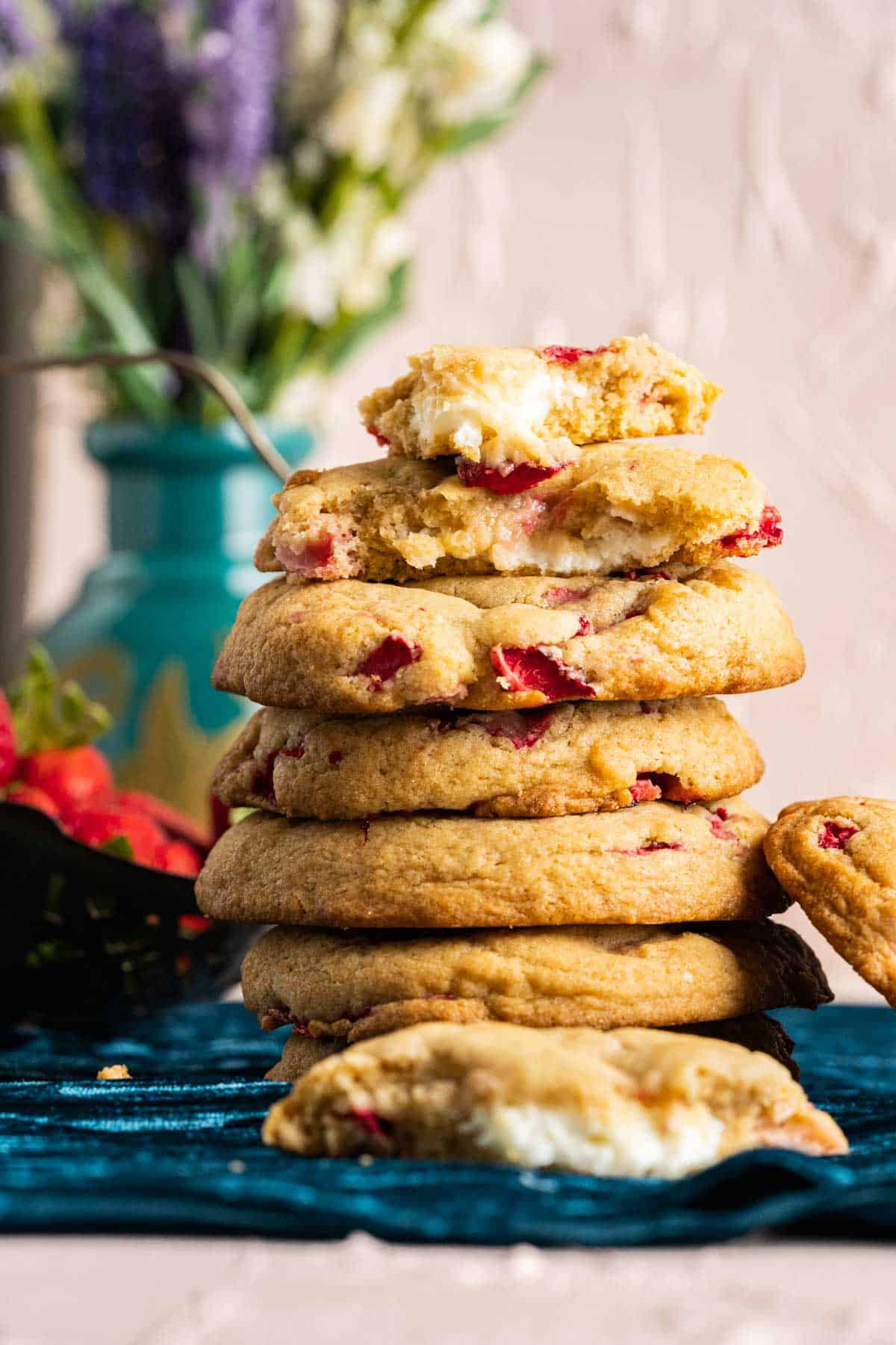 close shot of several strawberry creamcheese cookies stacked on each other with a flower vase in the backdrop.