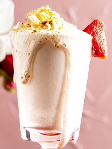 cheesecake milkshake in a tall glass with a strawberry on the side.