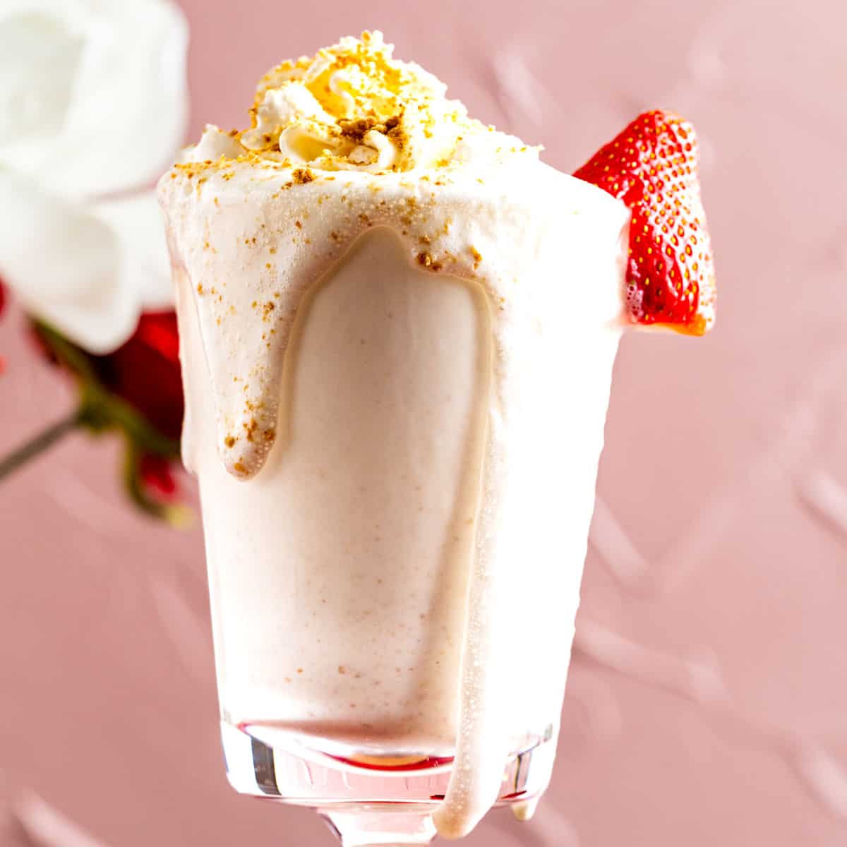cheesecake milkshake in a tall glass with a strawberry on the side.