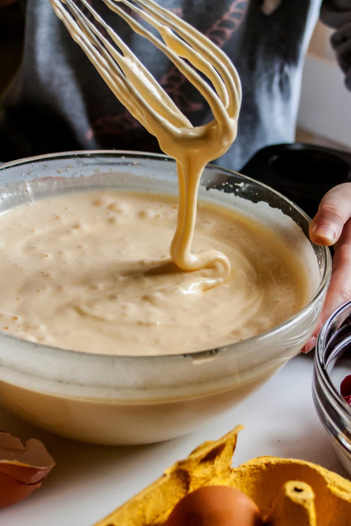 dripping cupcake batter from the whisk over a transparent bowl of cake batter.