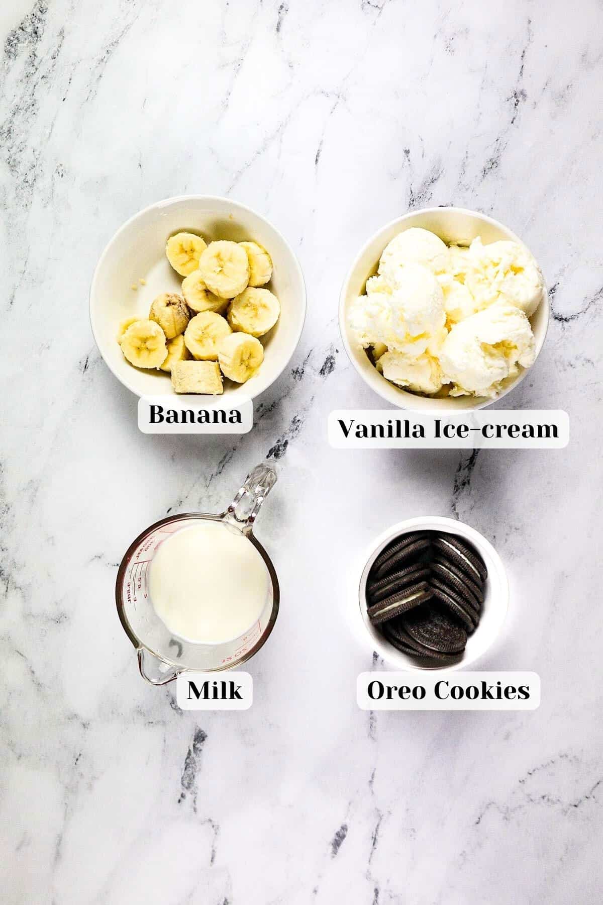 ingredients for the oreo banana milkshake set on the table on marble surface.