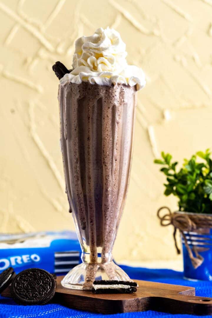 glass of milkshake with oreos scattered around on the table.
