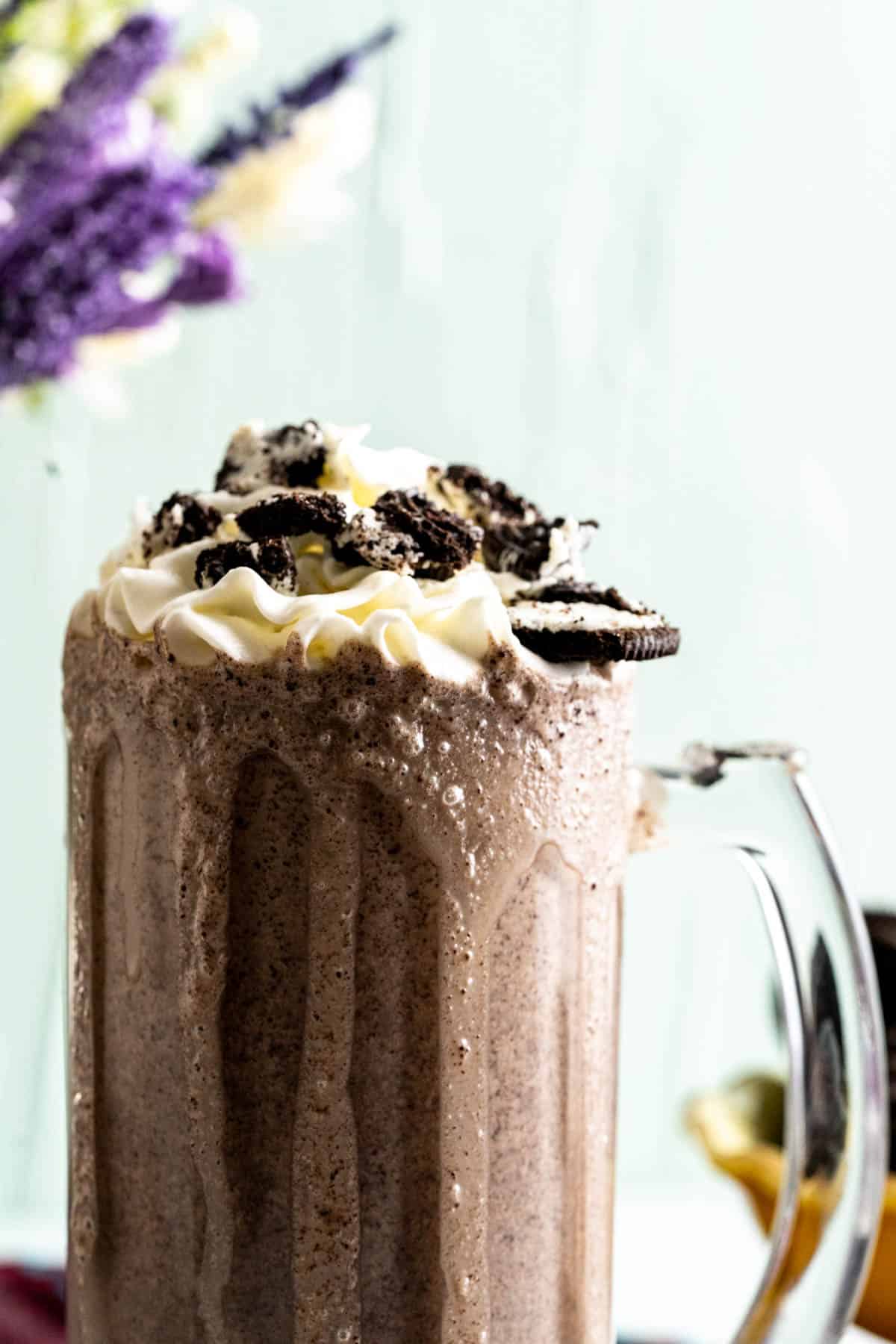 oreo shake in a tall transparent glass with crushed oreos on the top.
