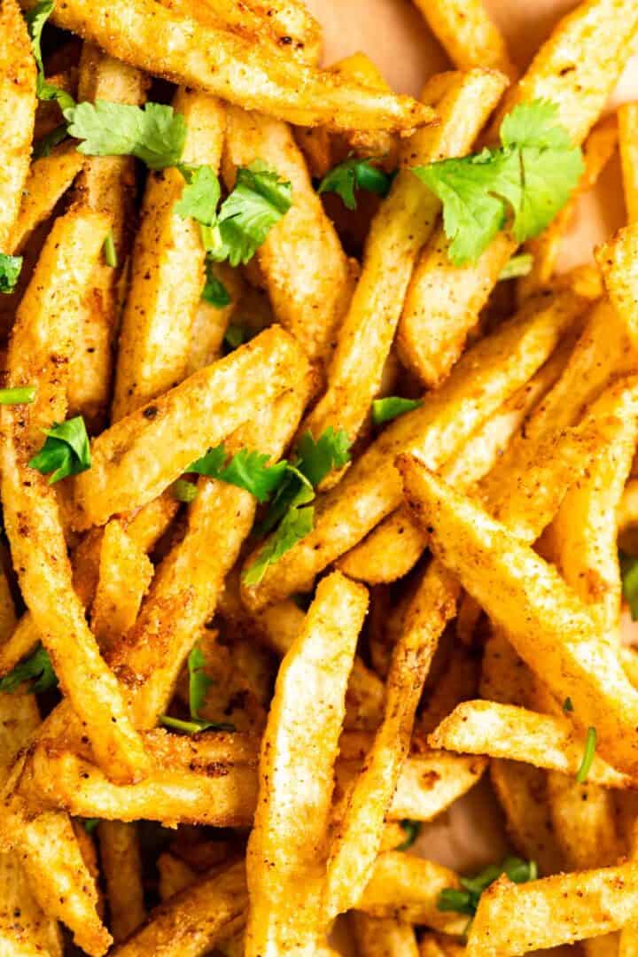 french fries on a brown paper with cilantro sprinkled over it.