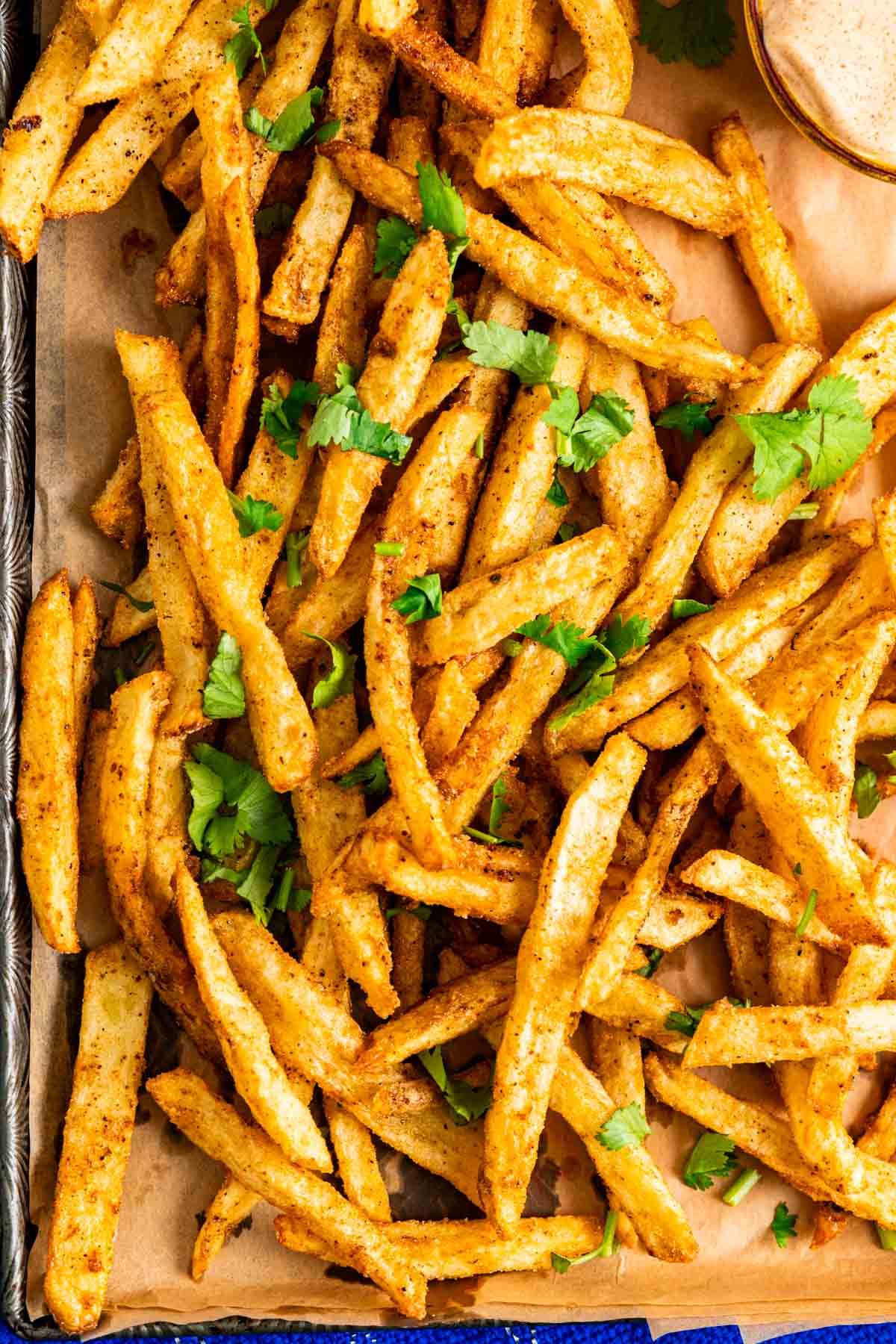 Masala fries spread on brown paper with coriander sprinkled on it. 