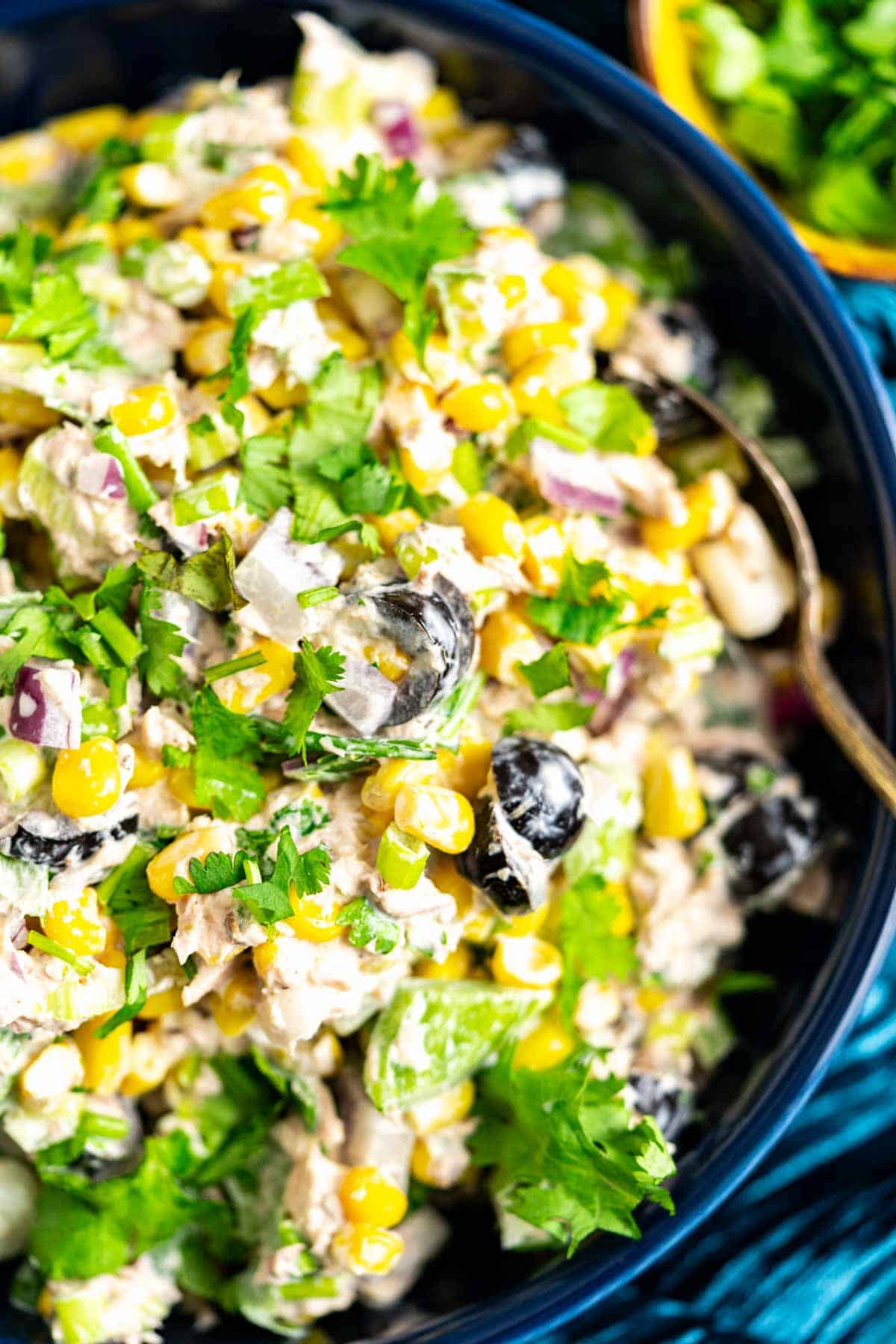 Tuna corn salad in a blue bowl with coriander leaves sprinkled on it. 