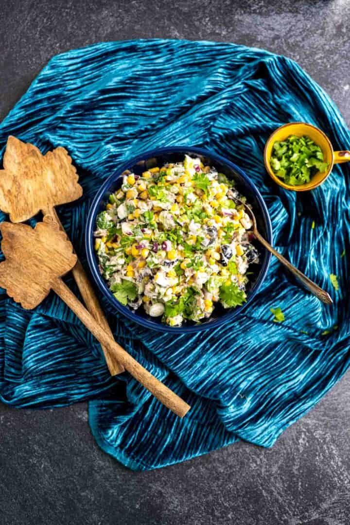 overhead shot of the tuna corn salad on a blue table cloth with two wooden spoons around.