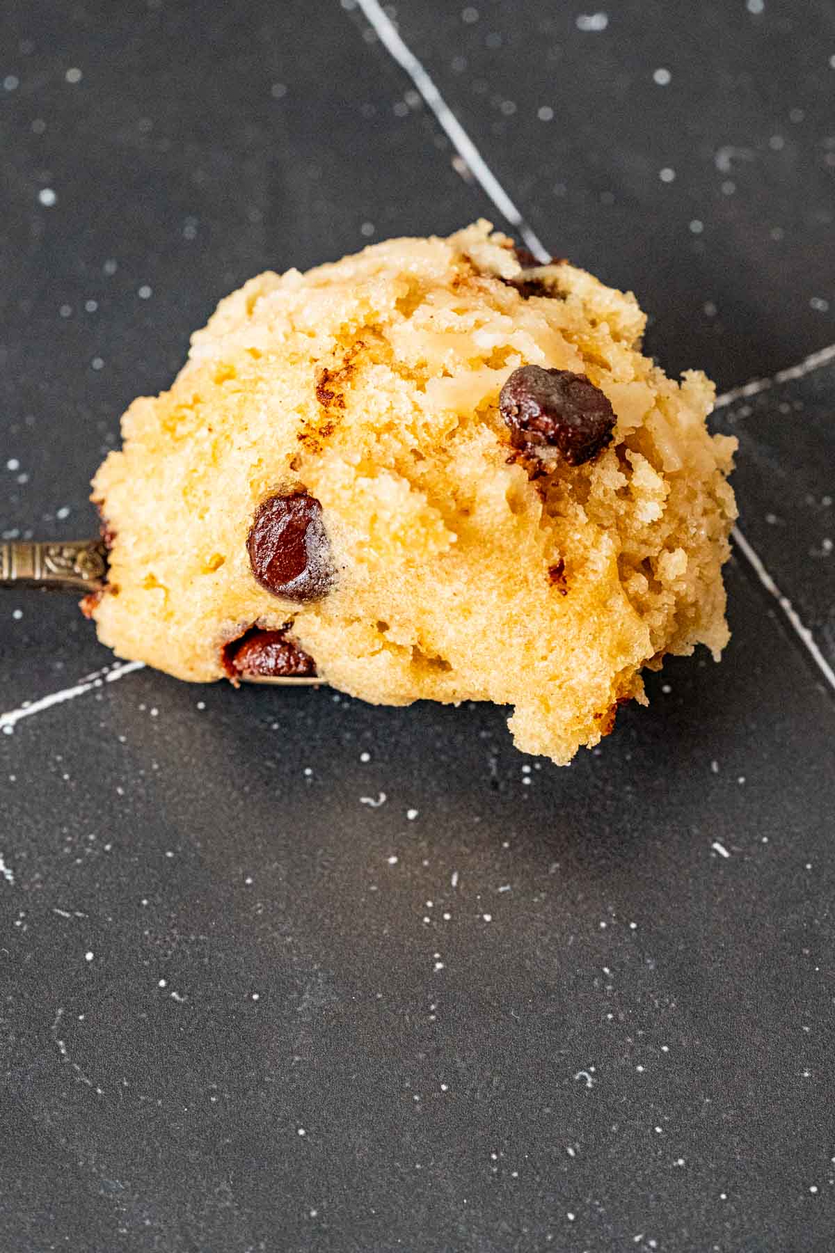 One bite of chocolate chip mug cake sitting on a silver spoon.