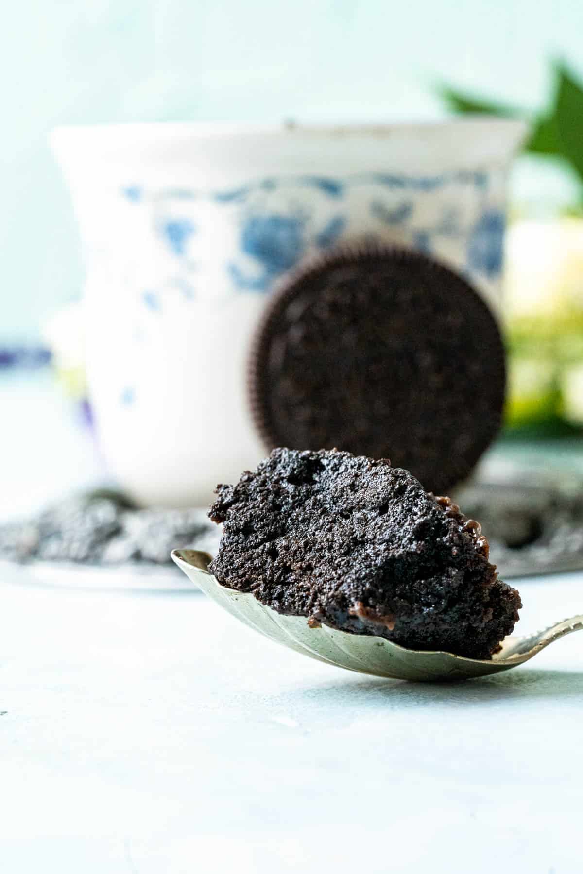 A bite of Oreo mug cake in a silver spoon sitting on a blue table.